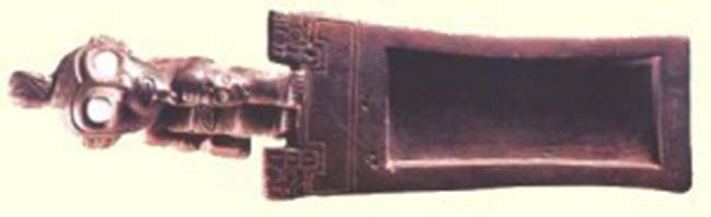 Tableta de madera con incrustaciones de turquesa en los ojos, usada para inhalar alucinógenos. Cultura Tiwanaku. Tomado de Tesoros de San Pedro de Atacama - Museo Chileno de Arte Precolombino.